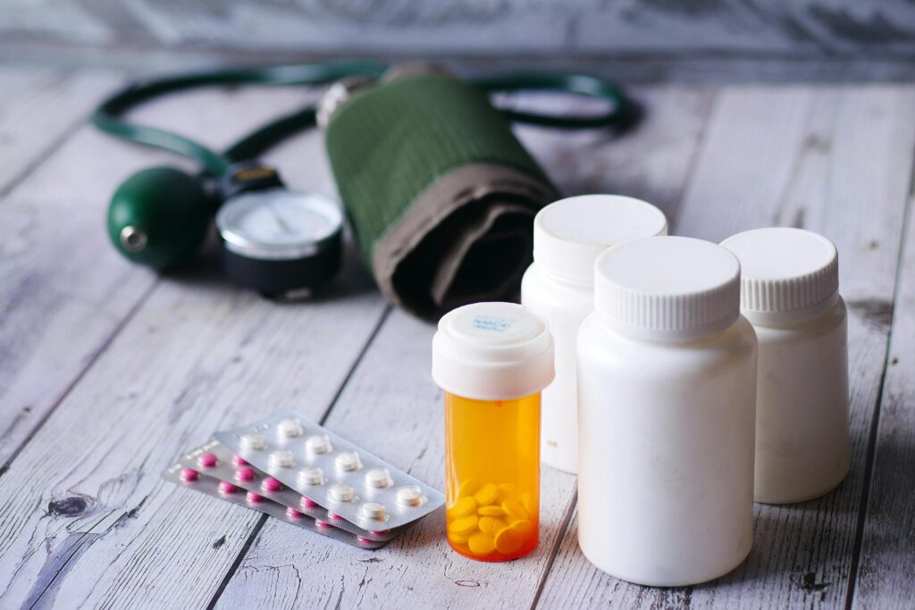 Prescription bottles, a blister pack of pills, and a blood-pressure cuff on a wooden table